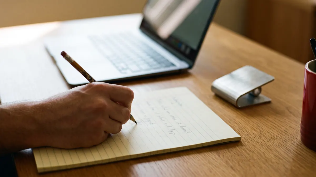 Mano escribiendo una lista de especificaciones en una libreta junto a una pieza de muestra