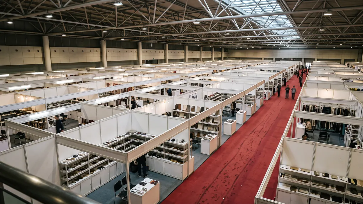 Interior de un enorme pabellón de exposiciones con una retícula de estands blancos vista desde arriba