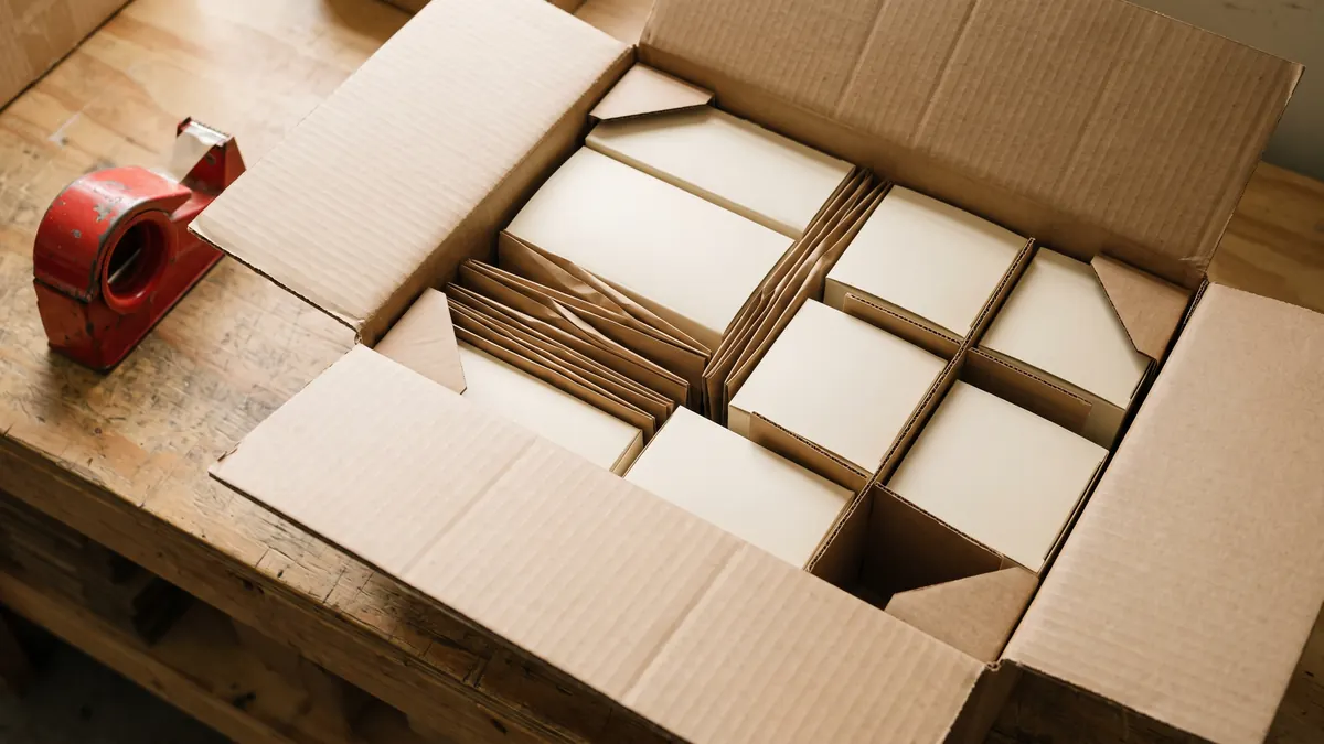 Caja máster abierta sobre un banco de empaque mostrando cajas interiores, separadores y esquineros