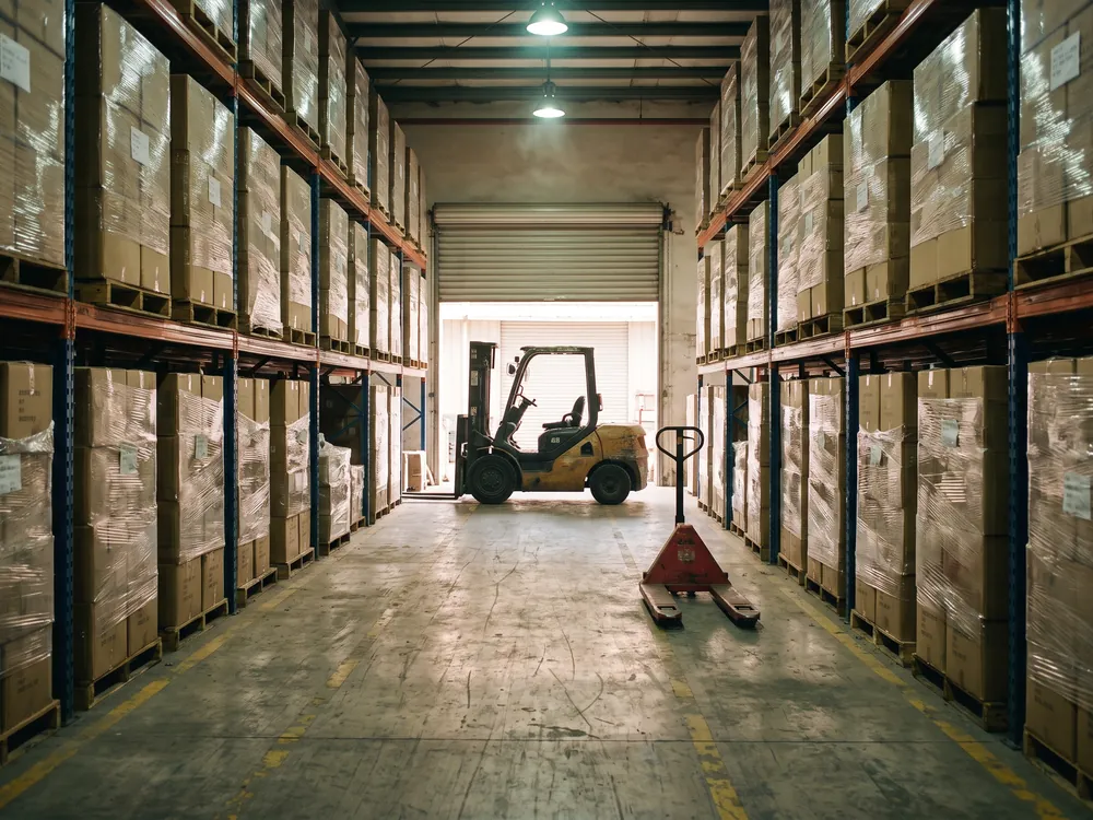 Pasillo de bodega de consolidación con tarimas emplayadas y un montacargas al fondo