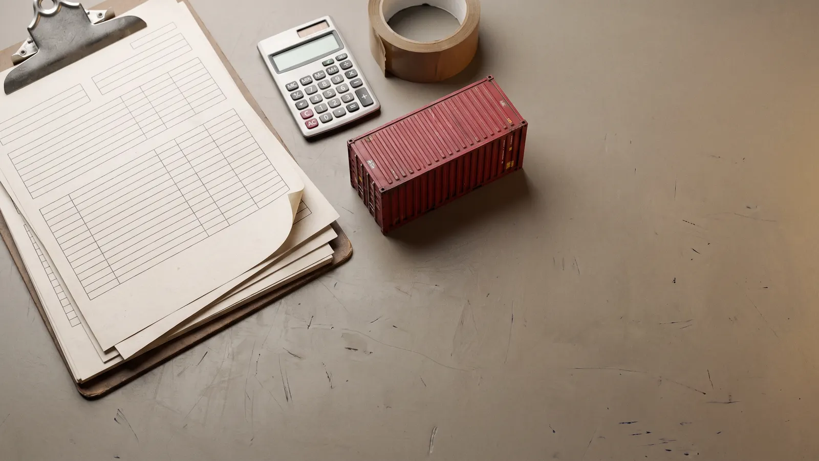 Vista cenital de papelería de importación sobre un escritorio: formularios en blanco, tablilla, calculadora y una maqueta de contenedor