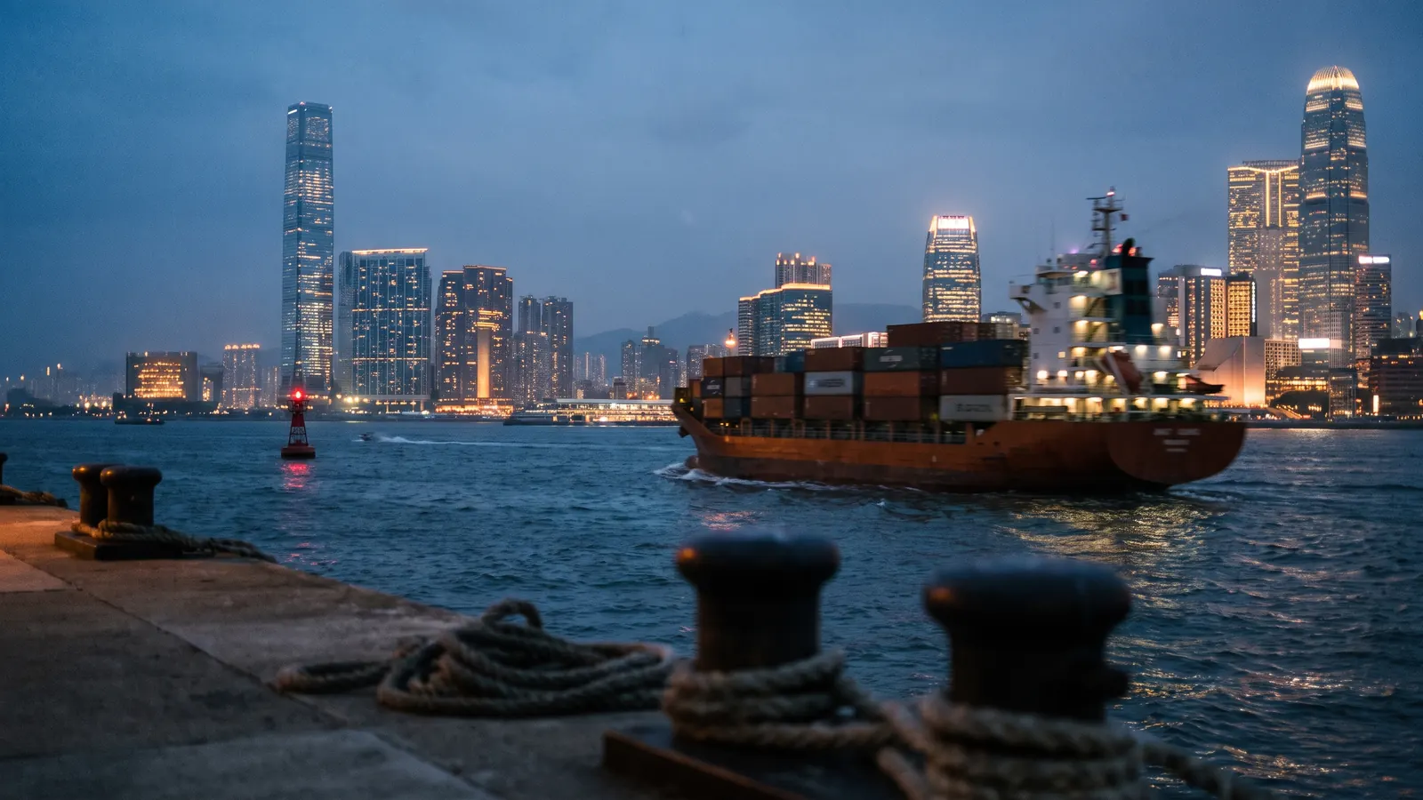 El puerto de Hong Kong al anochecer con un buque portacontenedores cruzando frente a la ciudad
